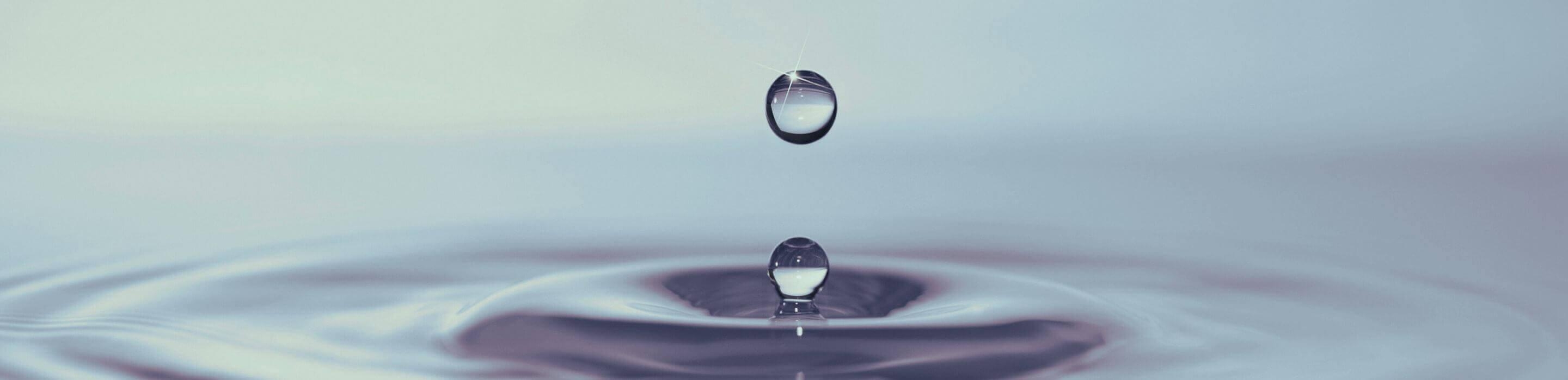 Water droplet creating ripples on a calm surface, symbolising how small actions create wider impact.